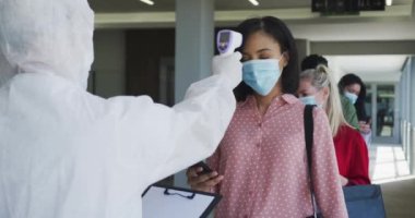 Gündelik ofiste çalışan çok ırklı bir grup, yüz maskeleri ile Covid 19 'u korumak için kuyrukta bekliyor. Coronavirus Covid 19 salgını sırasında iş yerindeki sıcaklığın yavaş çekim sosyal mesafesini kontrol ediyorlar.
