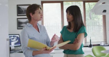 Gülümseyen melez kadın hasta modern diş kliniğinde dişçi kadın hemşireyle konuşuyor. Sağlık ve dişçilik sektörü.