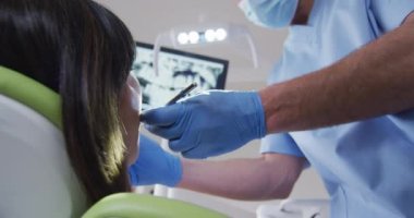 Modern diş kliniğinde kadın hastaların dişlerini inceleyen yüz maskeli beyaz erkek diş hekimi. covid 19 salgını sırasında sağlık ve dişçilik sektörü.
