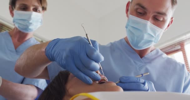 現代の歯科医院で女性患者の歯を調べるフェイスマスクを持つ白人男性歯科医 感染症の流行期における医療 歯科事業は — ストック動画