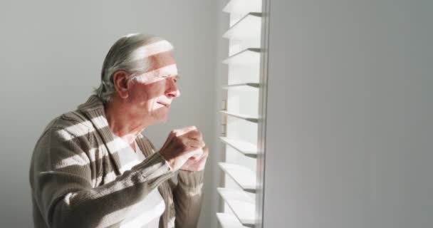 Sidovy Över Pensionerad Senior Man Kofta Tröja Tittar Genom Fönsterpersienner — Stockvideo