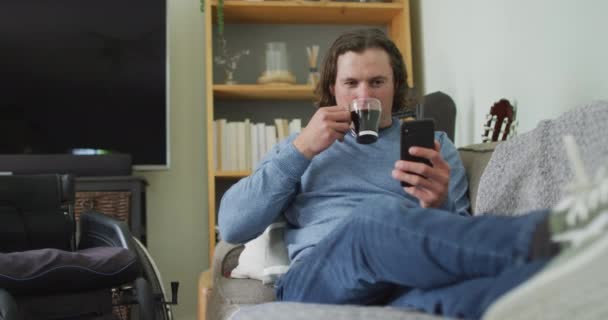 Szczęśliwy Biały Niepełnosprawny Mężczyzna Siedzi Kanapie Salonie Używając Smartfona Pijąc — Wideo stockowe