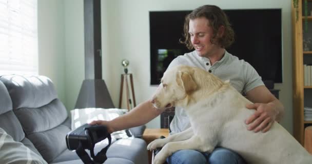 リビングでペット犬と遊んでいる車椅子で幸せな白人障害者 身体障害のある国内生活 — ストック動画