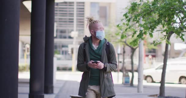 白化病非洲裔美国人 戴着面具 带着可怕的头发走路和使用智能手机 在科沃德大流行期间 在城市里四处游荡 — 图库视频影像