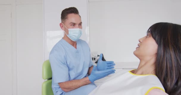 在现代牙科诊所 白种人男牙医戴着面罩 准备微笑的女病人 流行病蔓延期间的保健和牙科业务D — 图库视频影像
