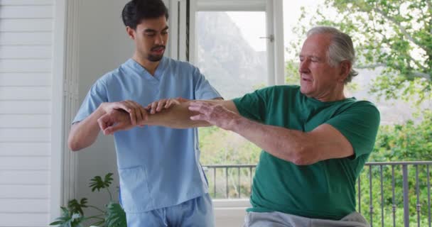 Langzame Beweging Van Biraciale Mannelijke Fysiotherapeut Die Arm Van Gepensioneerde — Stockvideo
