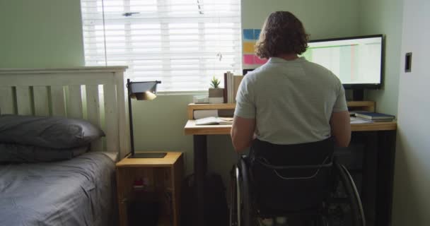 重点是坐在轮椅上的高加索残疾人和他的宠物狗在卧室里使用电脑 有身体残疾的家庭生活方式 — 图库视频影像