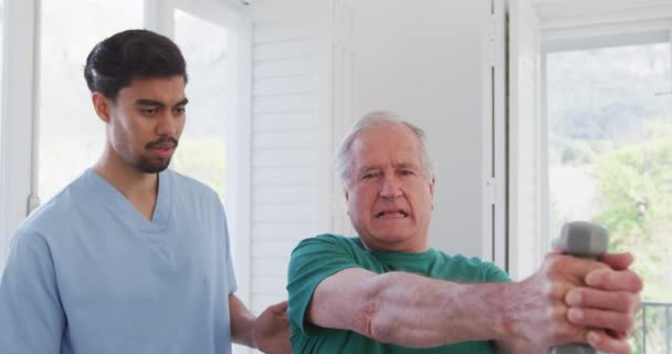 Terapeuta Masculino Biracial Conversando Com Homem Sênior Exercitando Com Halteres — Vídeo de Stock