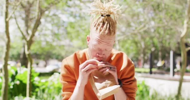Albino African American Man Dreadlocks Sitting Park Bike Eating Sandwich — Stock Video