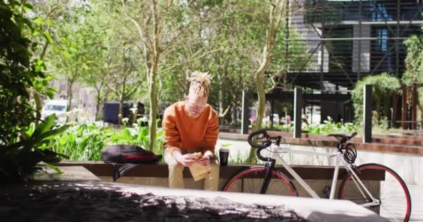 Ένας Αφροαμερικάνος Κοτσιδάκια Κάθεται Στο Πάρκο Και Τρώει Σάντουιτς Ποδήλατο — Αρχείο Βίντεο