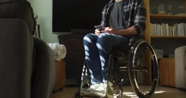 車いすの中の幸せな白人障害者は リビングルームでスマートフォンを使用しています 身体障害のある国内生活 — ストック動画