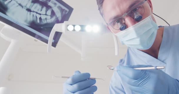 現代の歯科医院で歯を検査顔マスクを持つ白人男性歯科医 感染症の流行期における医療 歯科事業は — ストック動画