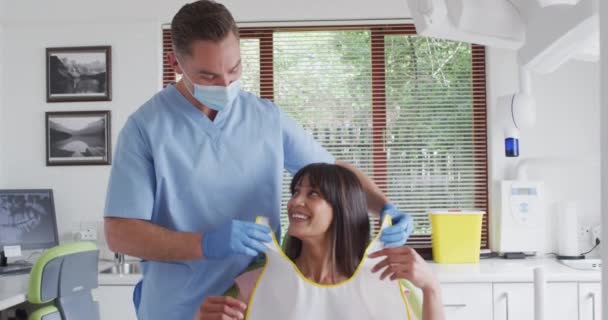 現代の歯科医院で笑顔の女性患者を準備フェイスマスクを持つ白人男性歯科医 感染症の流行期における医療 歯科事業は — ストック動画