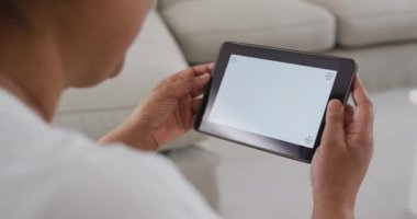 Afro-Amerikan son sınıf öğrencisi bir kadın kanepede oturup tablet kullanıyor ve ekranında kopya alanı var. Emeklilik hayatı, evde teknolojiyle baş başa zaman geçirmek..
