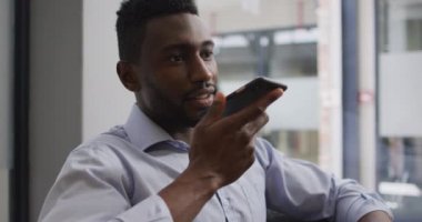Endişeli Afrikalı Amerikalı iş adamı koltuğunda oturmuş modern ofisteki akıllı telefondan konuşuyor. iş ve işyeri.
