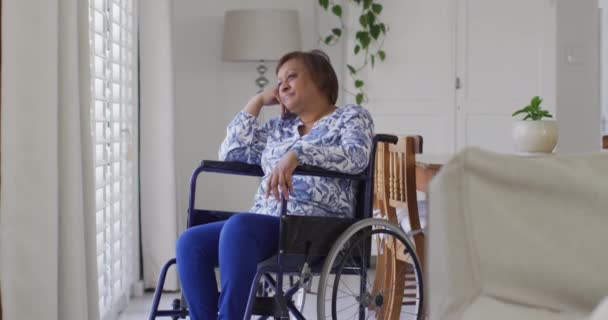笑顔で窓の外を見て車椅子で幸せなアフリカ系アメリカ人のシニア女性 退職生活や身体障害のある国内生活 — ストック動画