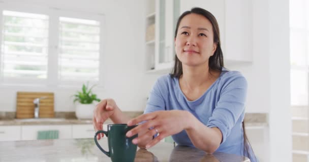 Ευτυχισμένη Ασιάτισσα Που Κάθεται Στην Κουζίνα Και Πίνει Καφέ Τρόπος — Αρχείο Βίντεο