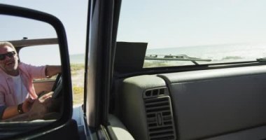 Mutlu beyaz erkek çift arabada oturuyor, harita okuyor ve sahilde akıllı telefon kullanıyor. Yaz gezisi ve doğada tatil.