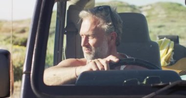 Güneşli bir günde plajda arabasında oturan düşünceli beyaz bir adam. Yaz gezisi ve doğada tatil.