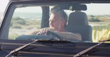 Güneşli bir günde plajda arabasında oturan düşünceli beyaz bir adam. Yaz gezisi ve doğada tatil.