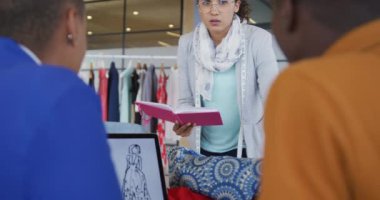 Çeşitli kadın ve erkek tasarımcılar stüdyoda dizüstü bilgisayarda moda tasarımlarını tartışıyor. İş ve teknoloji yaratıcı tasarım stüdyosunda.