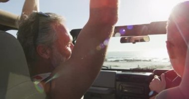 Mutlu beyaz erkek çift arabada oturuyor ve güneşli bir günde kumsalda beşlik çakıyor. Yaz gezisi ve doğada tatil.