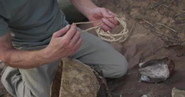Beyaz erkek hayatta kalma uzmanı, çöldeki kampta ateş yakmak için sicimden tutuşturmaya hazırlanıyor. Keşif, seyahat ve macera, doğada hayatta kalma uzmanı..