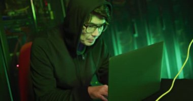 Bilgisayar sunucuları tarafından dizüstü bilgisayar kullanan kapüşonlu Asyalı erkek hacker. İnternet güvenliği, siber suç, bilgi teknolojisi, veri işleme ve bilgisayar sunucuları.