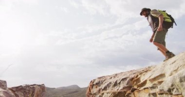 Sırt çantalı, beyaz sakallı, erkek, vahşi doğada kayalık dağ geçidinde atlıyor. Keşif, seyahat ve macera, doğada hayatta kalma uzmanı..