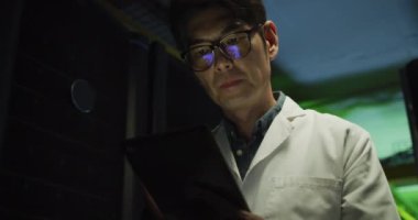 Asyalı erkek, laboratuvar önlüklü, tablet kontrol sunucusu kullanan teknisyen. bilgi teknolojisi, veri işleme ve bilgisayar sunucuları.