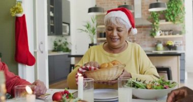 Noel Baba şapkalı bir grup mutlu kıdemli arkadaş evdeki Noel yemeği masasında yemek dağıtıyor. Emeklilik hayatı, Noel kutlamaları, arkadaşlarla evde kutlama..