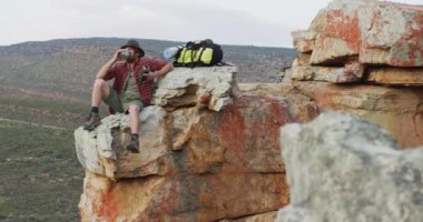 Beyaz erkek, kayalık dağların tepesinde oturuyor, dinleniyor ve su içiyor. Keşif, seyahat ve macera, doğada hayatta kalma uzmanı..