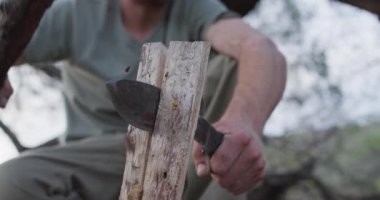 Beyaz erkek hayatta kalma uzmanı kampta yakacak odun kesmek için dal ve pala kullanıyor. Keşif, seyahat ve macera, doğada hayatta kalma uzmanı..