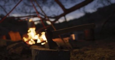 Akşamları vahşi doğadaki hayatta kalma kampında kükreyen bir kamp ateşinin önünde baltayla. Keşif, seyahat ve macera, doğada hayatta kalma uzmanı..