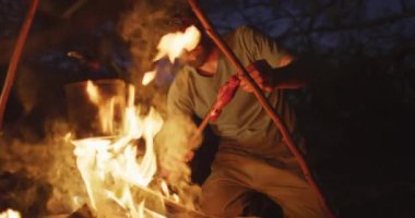 Sakallı, beyaz erkek, vahşi doğada hayatta kalıyor. Kamp ateşinde et pişiriyor ve ısıtıyor. Keşif, seyahat ve macera, doğada hayatta kalma uzmanı..