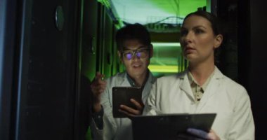 Çeşitli kadın ve erkek teknisyenler laboratuvar önlükleriyle tablet ve dizüstü bilgisayarlarını kontrol ediyorlar. bilgi teknolojisi, veri işleme ve bilgisayar sunucuları.