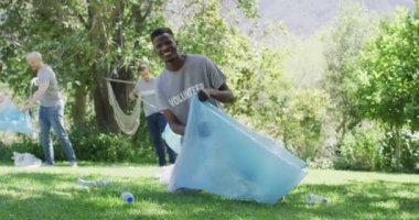 Gönüllü tişörtlü, atık poşetlerine dışarıda plastik atık koyan mutlu arkadaş grubu. Çevre koruma gönüllüleri kırsal alanda temizlik yapıyor..