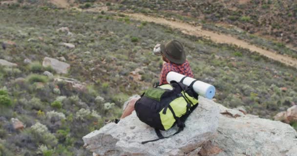 白人男性幸存者坐在荒原的岩石山顶上 休息和喝水 自然求生者 — 图库视频影像