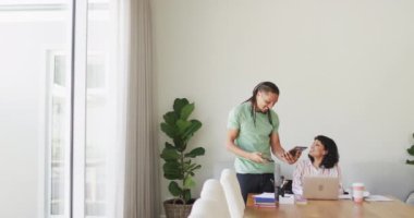 Tekerlekli sandalyedeki mutlu kadın oturma odasında dizüstü bilgisayar kullanıyor, tablet kullanan gülümseyen erkek partner. Fiziksel engelli refah ve ev hayatı.