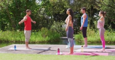 Kafkas erkek eğitmenin farklı gruplarla parkta yoga pozu verişi. fitness, sağlıklı hobiler ve açık havada aktif yaşam tarzı.