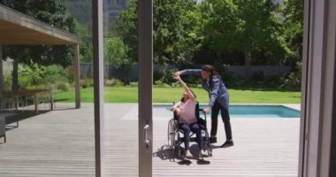 Bahçede dans eden tekerlekli sandalyedeki mutlu çift ırklı kadın. Rasta saçlı, gülümseyen erkek partnerle. Fiziksel engelli refah ve ev hayatı.