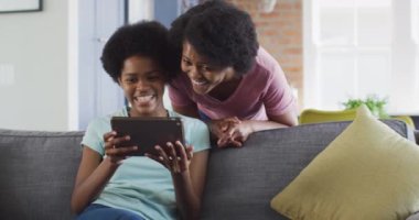 Mutlu Afro-Amerikan anne ve kızı tablet kullanarak kanepede oturuyor. evde aile hayatı ve kaliteli aile zamanı.
