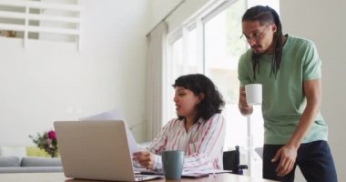 Tekerlekli sandalyedeki gülümseyen melez kadın ve erkek ortak oturma odasında dizüstü bilgisayar kullanarak evrak işleriyle uğraşıyorlar. Fiziksel engelli refah ve ev hayatı. 
