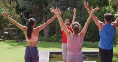 Çeşitli grup ve erkek eğitmen yoga yapıyor, ayakta duruyor ve güneşli parkta kollarını kaldırıyor. fitness, sağlıklı hobiler ve açık havada aktif yaşam tarzı.