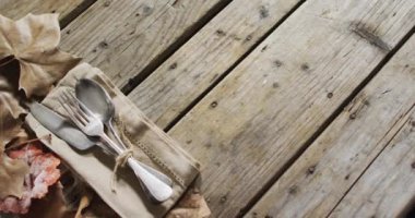 Ahşap yüzeyinde fotokopi alanı olan bir peçete ve sonbahar yapraklarının üzerine kurulmuş çatal bıçak takımının yakın görüntüsü. Şükran Günü şenliği konsepti