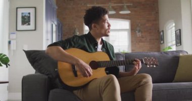 Oturma odasında oturup gitar çalan, şarkı söyleyen melez bir adam. Kaliteli zaman, evde dinlenme.