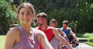 Güneşli parkta çeşitli gruplarla yoga yapan gülümseyen beyaz kadın. fitness, sağlıklı hobiler ve açık havada aktif yaşam tarzı.