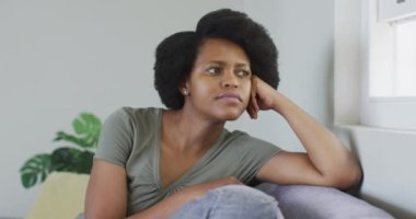 Düşünceli Afro-Amerikan kadın kanepede oturuyor, pencereden bakıyor. ev hayatı, evde zaman geçirmek..