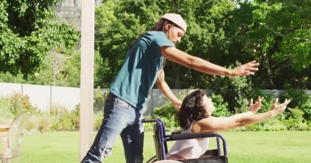 坐在轮椅上快乐的女人在花园里和有可怕头发的男伴跳舞 身体残疾的福祉和家庭生活方式 — 图库视频影像