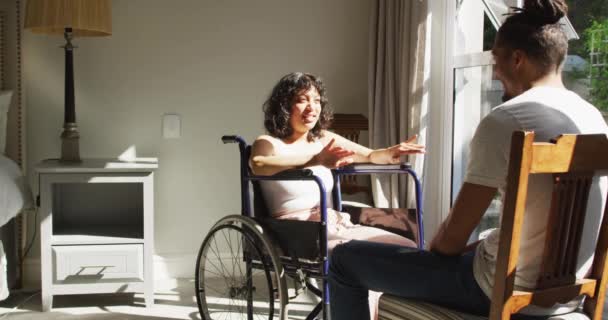 車椅子の妊婦と男性のパートナーが座って日当たりの良い部屋の窓のそばで話しています 身体障害者の健康と国内生活 — ストック動画